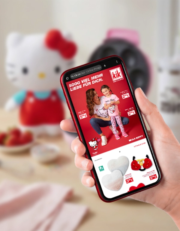 Hand hält Smartphone mit Hello Kitty Werbung, pinkes Waffeleisen und Snacks auf dem Tisch