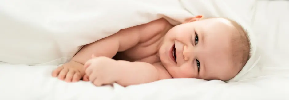 Eine Nahaufnahme eines Babys, das gemütlich unter einer flauschigen weißen Decke liegt und seine kleinen Hände und Füße zeigt.