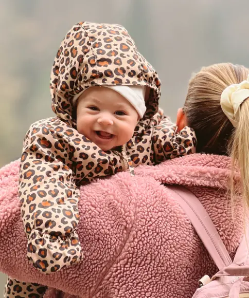 Eine Mutter hält ihr Baby, welches in einem Skianzug mit Leopardenmuster steckt