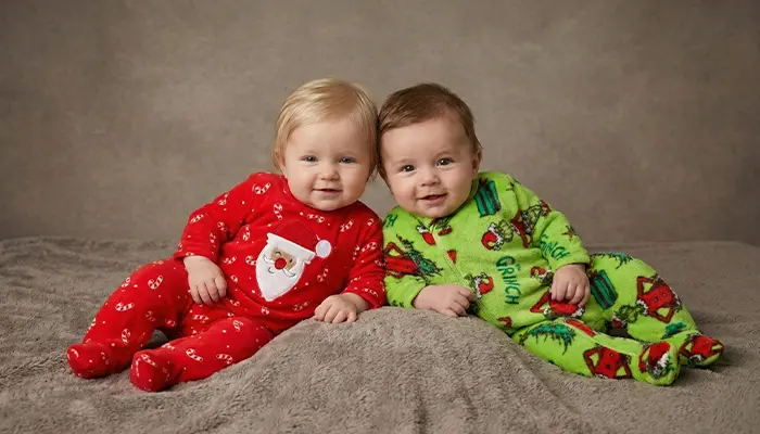 Zwei Babys in bunten Schlafanzügen liegen nebeneinander auf einer Decke.