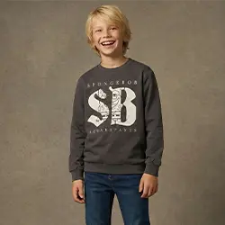 Junge in grauem Sweatshirt und Jeans lächelt vor neutralem Hintergrund.