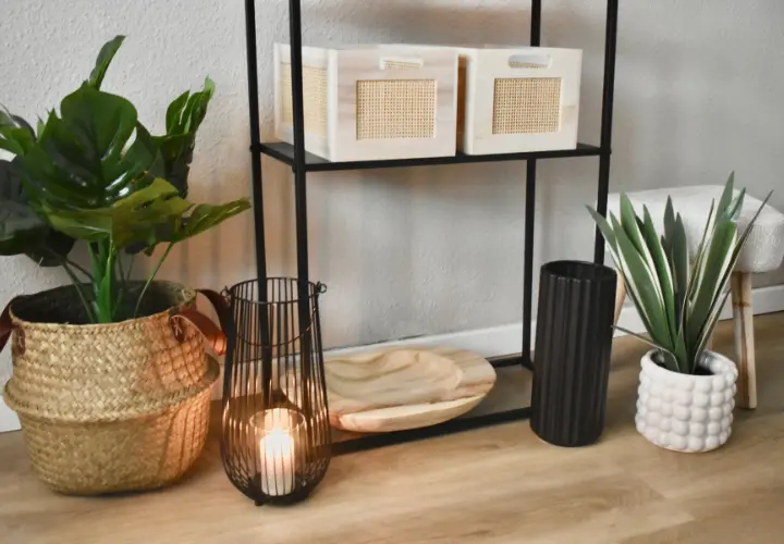 Ein stilvolles Regal präsentiert geflochtene Aufbewahrungsboxen, ein Holztablett, einen Kerzenhalter aus Metall und Topfpflanzen vor einer neutralen Wand.