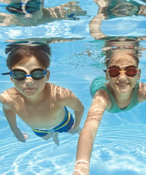 Ein Junge und ein Mädchen tragen Badebekleidung mit Taucherbrille und lächeln in die Kamera