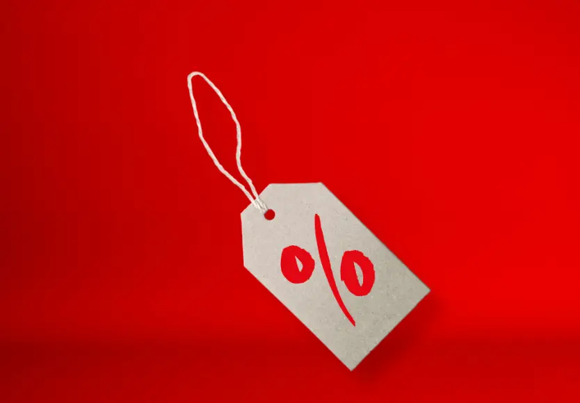 Ein graues Preisschild mit einem roten Prozentzeichen auf einem leuchtend roten Hintergrund, das Rabatte oder Sonderangebote symbolisiert.