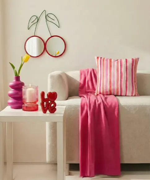 Stilvolles Wohnzimmer mit Sofa, pinker Deko, Kissen, Decke und Kerzen im modernen Design