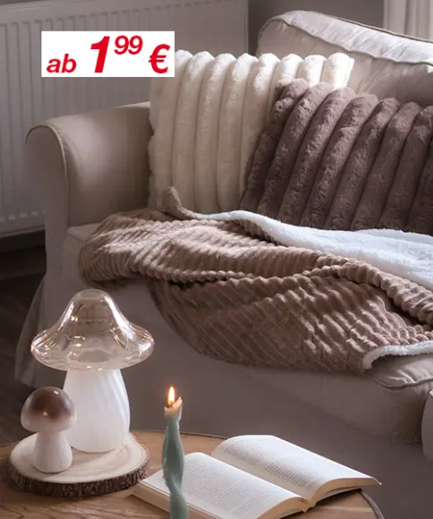 Gemütliche Wohnzimmerszene mit weichen Kissen, flauschigen Decken, einer leuchtenden Kerze und einer Pilzlampe auf einem Holztisch.