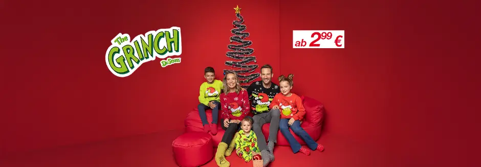 Eine Familie in bunten Weihnachtspullovern posiert auf roten Sitzsäcken vor einem festlich geschmückten Baum vor einem passenden roten Hintergrund.