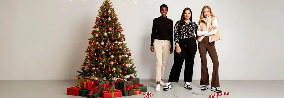 Drei Frauen posieren gemeinsam vor einem wunderschön geschmückten Weihnachtsbaum mit Geschenken und sorgen so für eine festliche Weihnachtsstimmung.