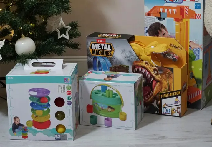 Eine Sammlung bunter Kinderspielzeuge: Stapelringe, ein Spielset und ein Dinosaurier-Spiel, arrangiert neben einem geschmückten Weihnachtsbaum. Eine Sammlung bunter Kinderspielzeuge: Stapelringe, ein Spielset und ein Dinosaurier-Spiel, arrangiert neben einem geschmückten Weihnachtsbaum.