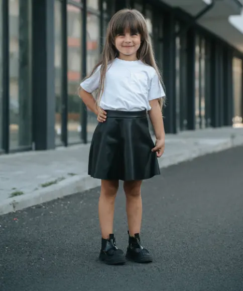 Ein kleines Mädchen mit einem schlichten weißen T-Shirt und einem schwarzen Minirock lächelt in die Kamera