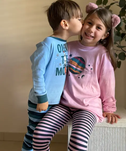 Ein Bruder und eine Schwester tragen ähnliche Pyjamas in blau und rosa und umarmen sich ganz fest.