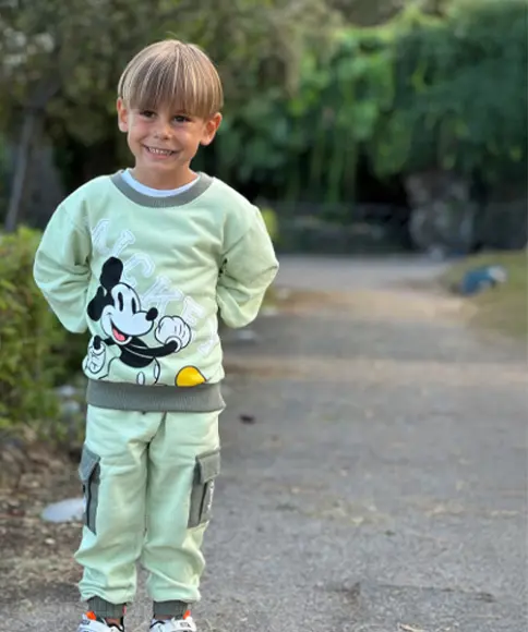 Ein kleiner Junge in einem Park trägt ein sportliches hellgrünes Set mit einem großen Mickey Maus Aufdruck