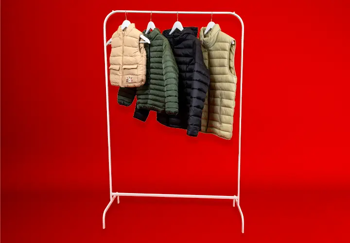 Ein weißer Kleiderständer zeigt vier Steppwesten in verschiedenen Farben – Beige, Dunkelgrün, Marineblau und Oliv – vor rotem Hintergrund.