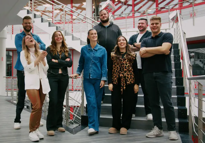Eine vielfältige Gruppe von acht Personen posiert auf einer Treppe in einem modernen Gebäude und vermittelt dabei eine entspannte, aber dennoch professionelle Atmosphäre.