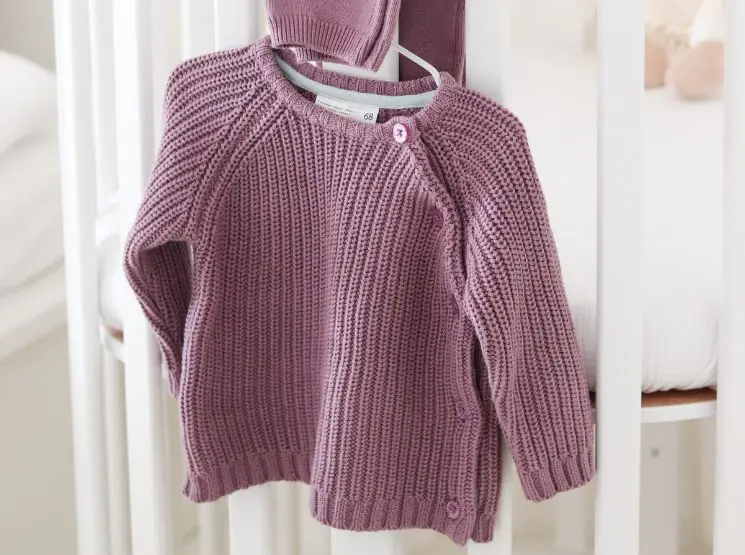 Ein Baby-Sweater hängt an einem Kleiderständer.