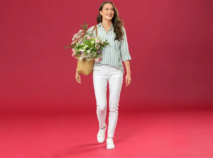 Eine Person in einem gestreiften Hemd und einer weißen Hose hält einen Korb mit bunten Blumen in der Hand.