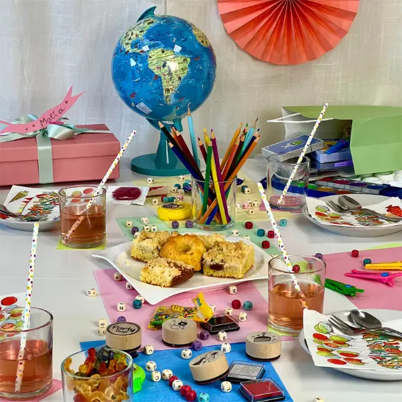 Ein bunt gedeckter Tisch mit einer Weltkugel, Snacks, Getränken und Malutensilien schafft eine festliche und kreative Atmosphäre für eine Zusammenkunft.