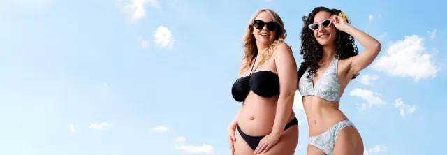 Zwei Frauen posieren selbstbewusst in Bikinis vor einem strahlend blauen Himmel und zelebrieren Körperbewusstsein und Sommerstimmung.