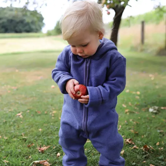 Frischer Wind im Kleiderschrank! Ein Kleinkind in einem blauen Strampler steht auf einer Wiese und hält Äpfel inmitten einer malerischen Parklandschaft in den Händen. Das Preisschild ist in der Ecke zu sehen.