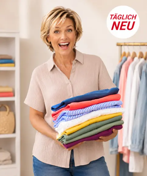 Person hält einen bunten Stapel gefalteter Kleidung in einem gemütlichen Raum mit Kleiderstange und Regalen im Hintergrund sowie dem Schriftzug „Täglich Neu“.