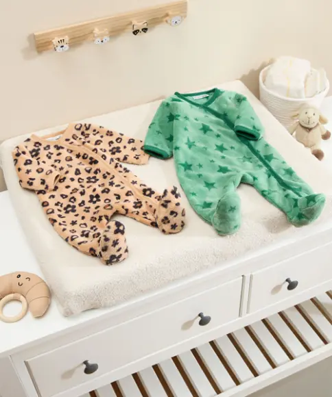 Auf einem Wickeltisch sind zwei süße Strampler ausgelegt