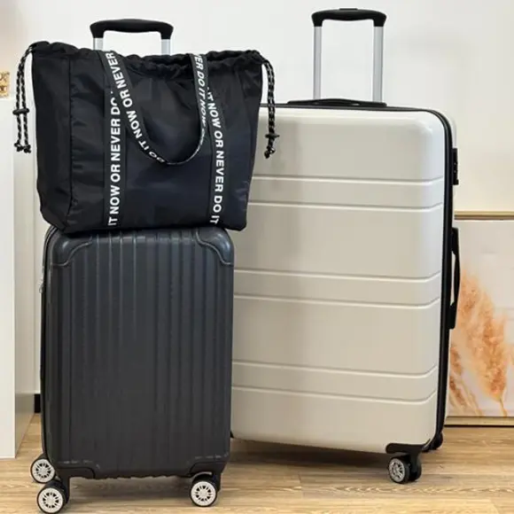 Eine schwarze Tasche mit Kordelzug sitzt auf einem schwarz-silbernen Koffer, der neben einem weißen Koffer in einem stilvollen Reise-Setup angeordnet ist.