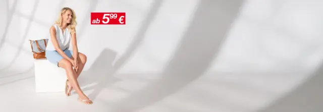 Eine Frau trägt eine leichte, sommerliche Bluse mit einer Jeansshorts und lächelt glücklich.