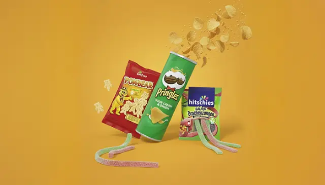 Bunte Snackauswahl vor gelbem Hintergrund mit Chipsdose, Gummibärchen und sauren Fruchtstreifen.