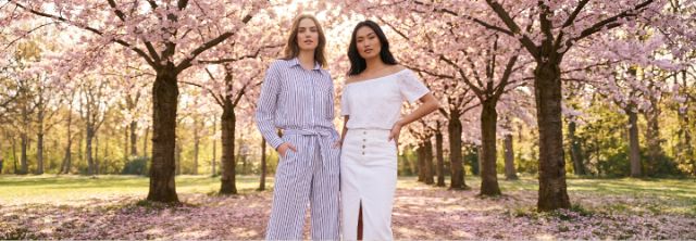 Zwei Frauen präsentieren moderne Damenmode unter blühenden Bäumen – frische Frühlingslooks für stilvolle und feminine Outfits