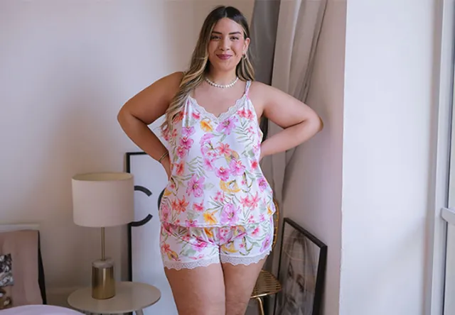 Eine Person steht selbstbewusst in einem blumengemusterten Pyjama-Set, mit sanfter Beleuchtung und gemütlicher Schlafzimmeratmosphäre.