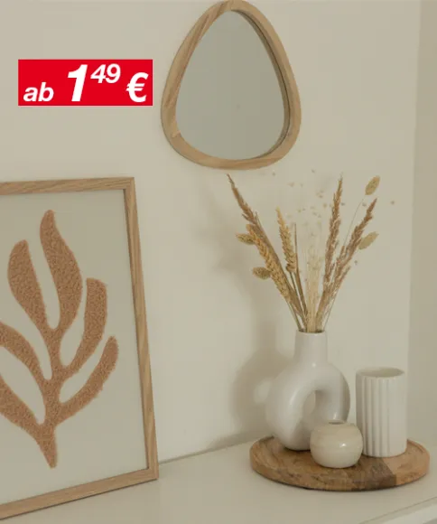 Eine minimalistische Einrichtung mit einem kleinen Spiegel, einem gerahmten Blattkunstwerk und einer Vase mit Trockenblumen auf einem Holztablett vor einer neutralen Wand.