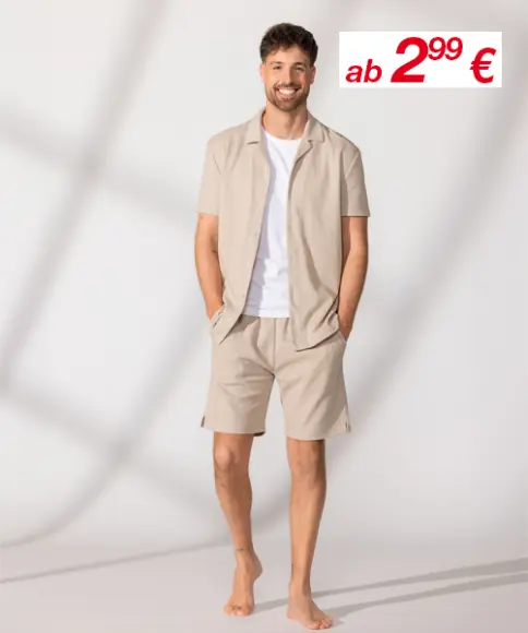 Ein Mann steht lässig in einem hellbeigen Kurzarmhemd und passenden Shorts und präsentiert ein entspanntes Sommeroutfit.