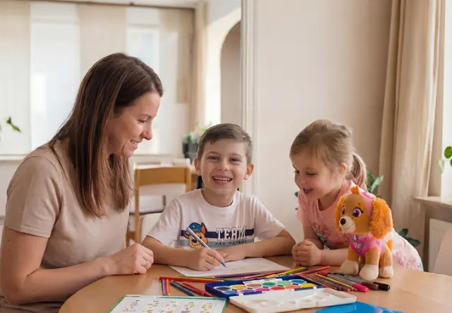Eine Frau malt gemeinsam mit zwei Kindern am Tisch. Buntstifte, Wasserfarben und ein PAW-Patrol-Plüschtier liegen bereit und laden zum kreativen Gestalten ein. Eine Frau malt gemeinsam mit zwei Kindern am Tisch. Buntstifte, Wasserfarben und ein PAW-Patrol-Plüschtier liegen bereit und laden zum kreativen Gestalten ein.