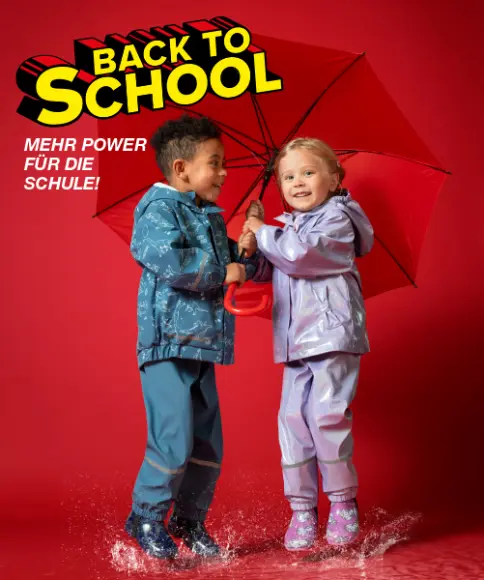 Zwei Kinder in bunten Regenmänteln planschen fröhlich in Pfützen, während sie sich einen leuchtend roten Regenschirm teilen.