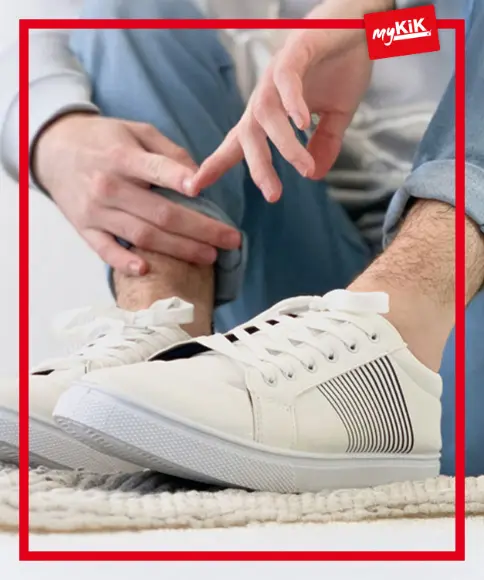 Eine Person in weißen Turnschuhen rückt die Manschette ihrer Hose zurecht und präsentiert einen lässigen Stil auf einer strukturierten Oberfläche.