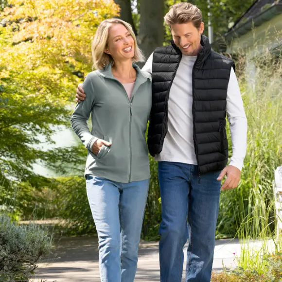 Ein Paar genießt einen Spaziergang im Freien, umgeben von Grün und Bäumen, beide lässig und bequem gekleidet.