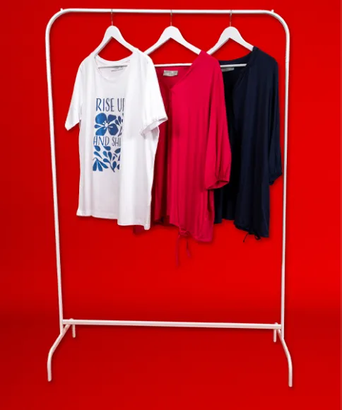 Drei stilvolle Oberteile auf einem weißen Kleiderständer: ein weißes T-Shirt mit Grafikdruck, eine rosa Bluse und ein marineblaues Top vor einem kräftig roten Hintergrund.