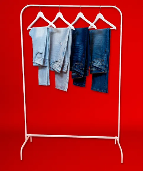 Ein weißer Kleiderständer präsentiert vier Jeans in verschiedenen Blautönen vor einem leuchtend roten Hintergrund.