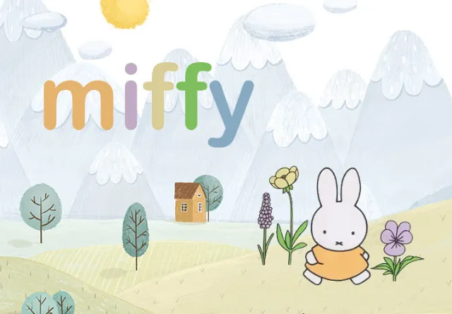 Der kleine Hase Miffy befindet sich auf einer Wiese mit Blumen und Bäumen. Im Hintergrund steht ein Haus und die Berge sind zu sehen.