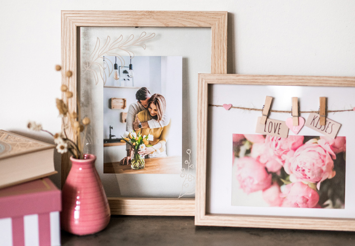 Eine gemütliche Auslage mit gerahmten Fotos und einer rosa Vase mit Blumen und dekorativen Schachteln