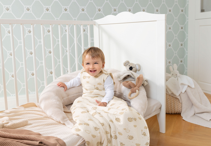 Ein Kleinkind in einem kuscheligen Schlafsack sitzt bequem in einem Kinderzimmer mit Plüschtieren. Ein Kleinkind in einem kuscheligen Schlafsack sitzt bequem in einem Kinderzimmer mit Plüschtieren.