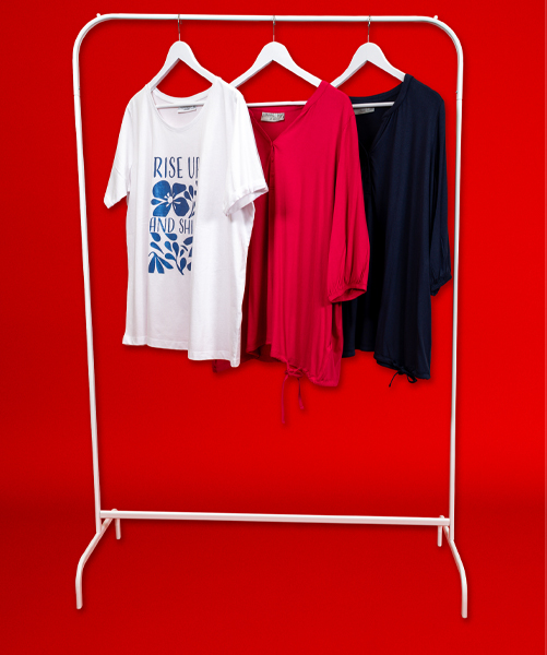 Drei stilvolle Oberteile auf einem weißen Kleiderständer: ein weißes T-Shirt mit Grafikdruck, eine rosa Bluse und ein marineblaues Top vor einem kräftig roten Hintergrund.