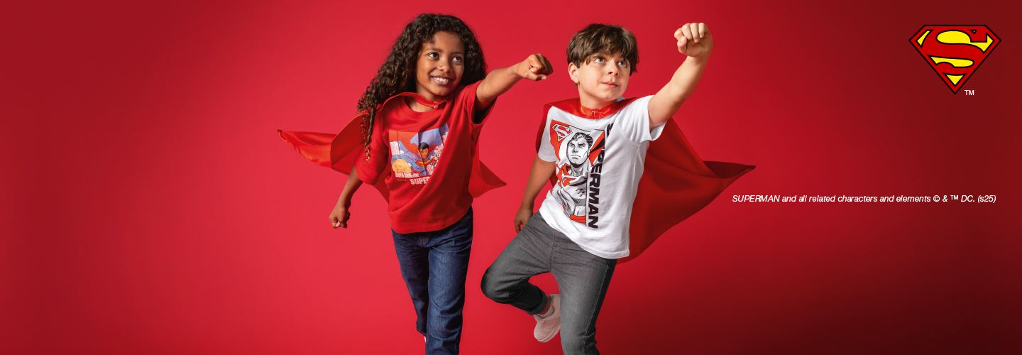 Zwei Kinder in Superheldenumhängen posieren selbstbewusst vor rotem Hintergrund und zeigen spaßige Superman-Outfits.