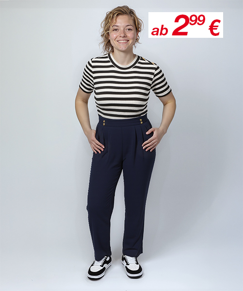 Eine Person steht selbstbewusst in einem gestreiften Shirt und einer hoch taillierten marineblauen Hose, kombiniert mit schwarz-weißen Schuhen, vor einem schlichten Hintergrund.