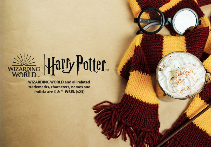 Harry Potter Logo und gelb, burgund farbener Schal, Brille und eine Kaffespezialität vor einem beigefarbenen Hintergrund