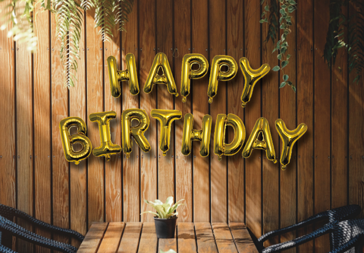Goldene Luftballons mit dem Spruch „Happy Birthday“ an einer Holzwand