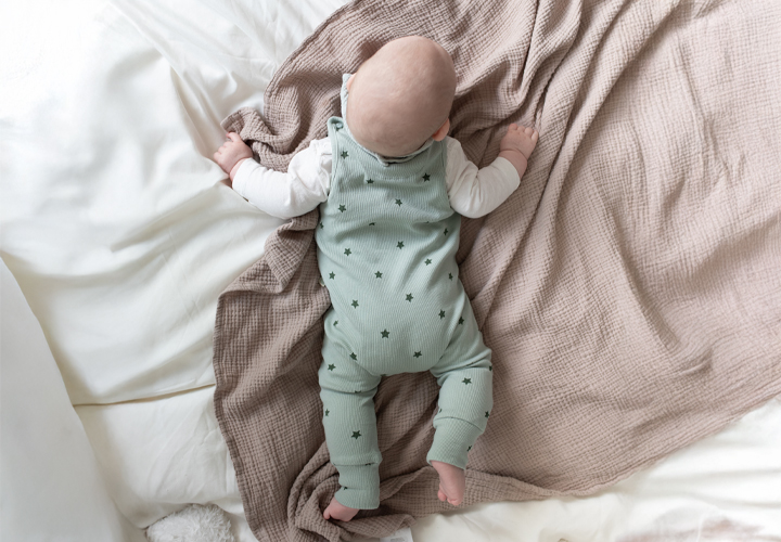 Ein Baby in einem grünen Sternenkostüm liegt auf einer weichen, strukturierten Decke und ruht friedlich in einem weißen Bett.