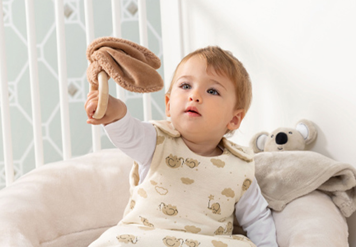 Ein kleines Kind, das einen kuscheligen Schlafsack trägt, sitzt auf einem Plüschsessel und hält einen weichen Plüschpilz hoch. Ein kleines Kind, das einen kuscheligen Schlafsack trägt, sitzt auf einem Plüschsessel und hält einen weichen Plüschpilz hoch.